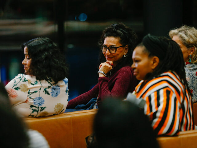 An audience image featuring 4 women in colourful clothing. 1 woman faces the camera with her hand under her chin, smiling